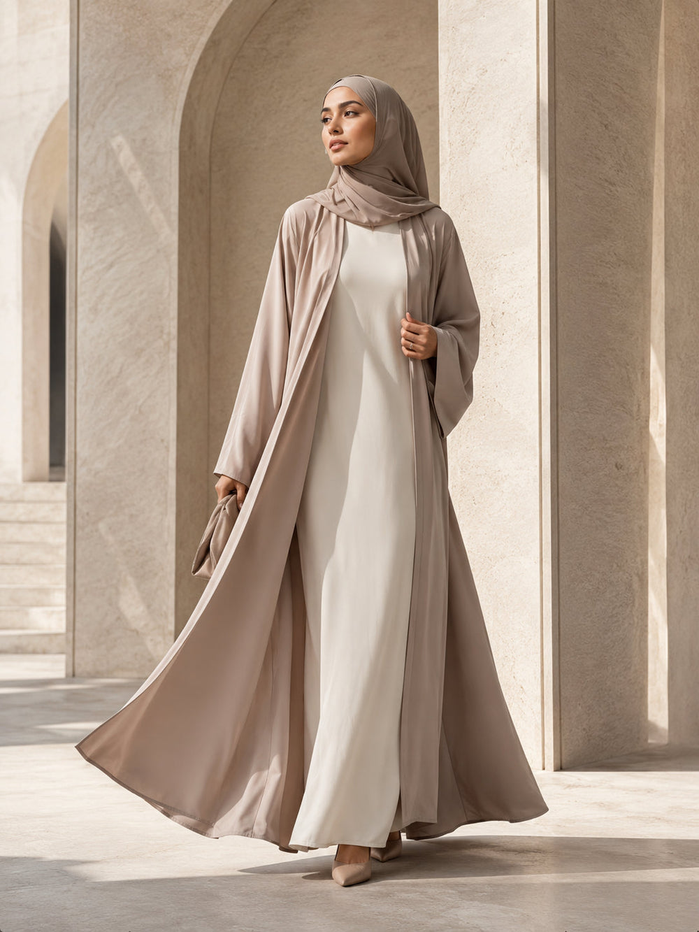 Model wearing tonal neutral layers with an open abaya in a limestone architectural setting