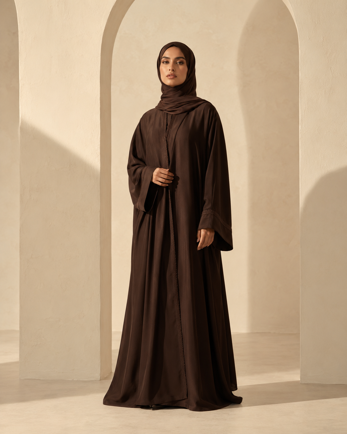 Woman in a chocolate brown abaya and matching hijab in a warm architectural studio collection at Neeim