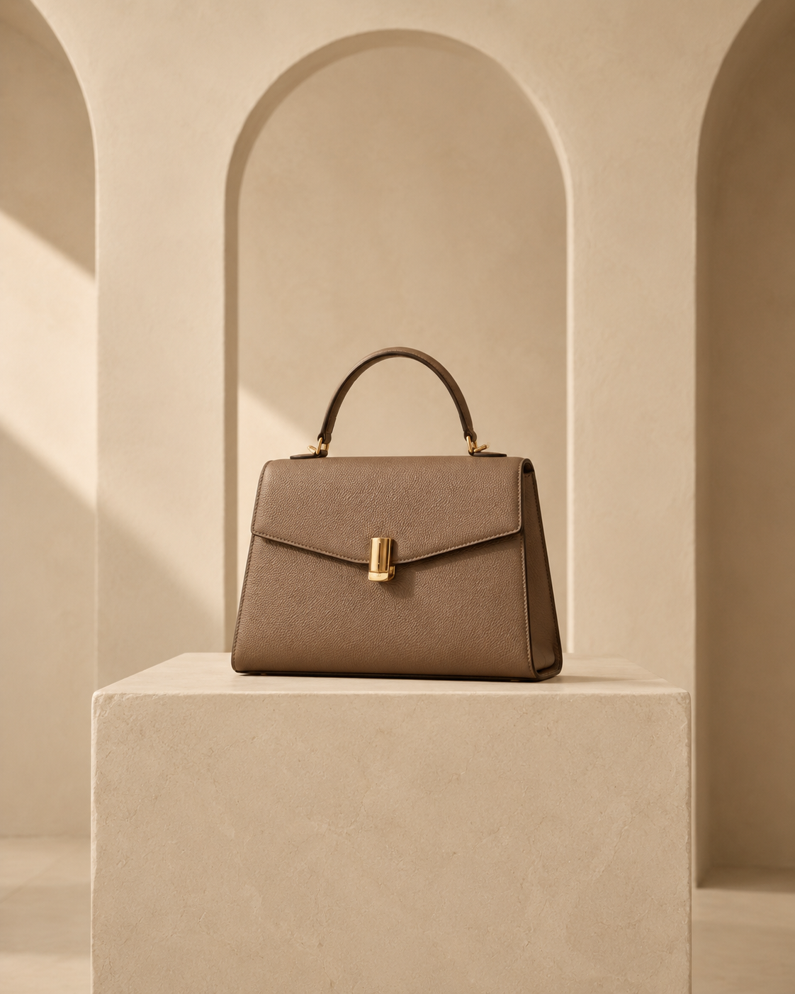 Taupe structured handbag on a limestone pedestal in a warm architectural studio collection at Neeim
